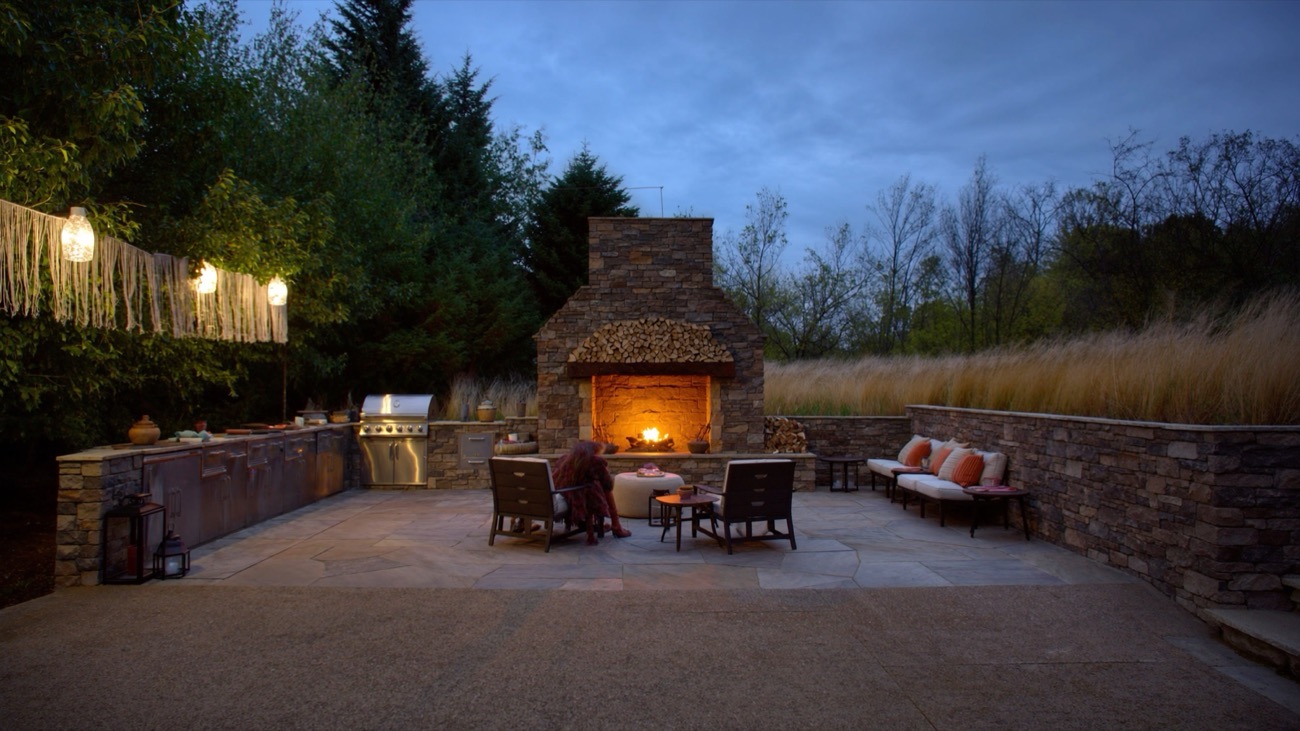 Outdoor stone fireplace and kitchen at dusk